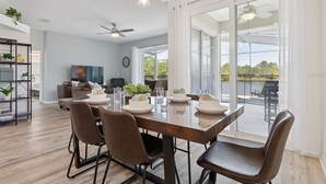 Un comedor con una mesa dispuesta para cuatro personas, un ventilador de techo y vistas a un lago a través de grandes puertas corredizas de vidrio.
