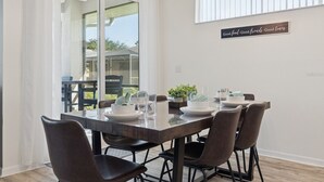 Un comedor con una mesa de vidrio, seis sillas y un letrero en la pared.