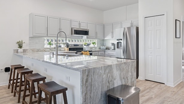 Una cocina moderna con muebles blancos, una isla central, electrodomésticos de acero inoxidable y taburetes de madera.