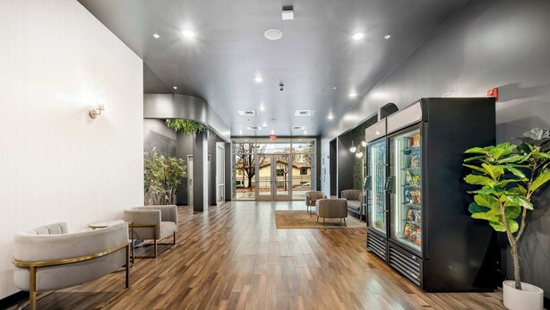 A modern hotel lobby with wooden flooring, seating areas, a refrigerator, and a large window. - Stylish 2B2B Apartment in Downtown ATL (Atlanta)