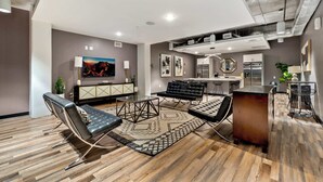 Ein modernes Wohnzimmer mit einer Couch, einem Couchtisch und einem Teppich. Es gibt eine Küchenzeile mit einem Kühlschrank und einem Esstisch.
