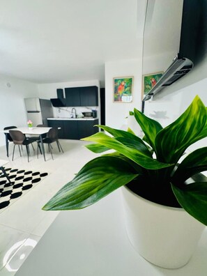 A modern living space with a dining area, kitchen, and a large potted plant.