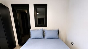 Ein Zimmer mit einem Einzelbett, einer hellblauen Tagesdecke, zwei Kissen, einem weißen Handtuch und einem schwarzen Kleiderschrank.