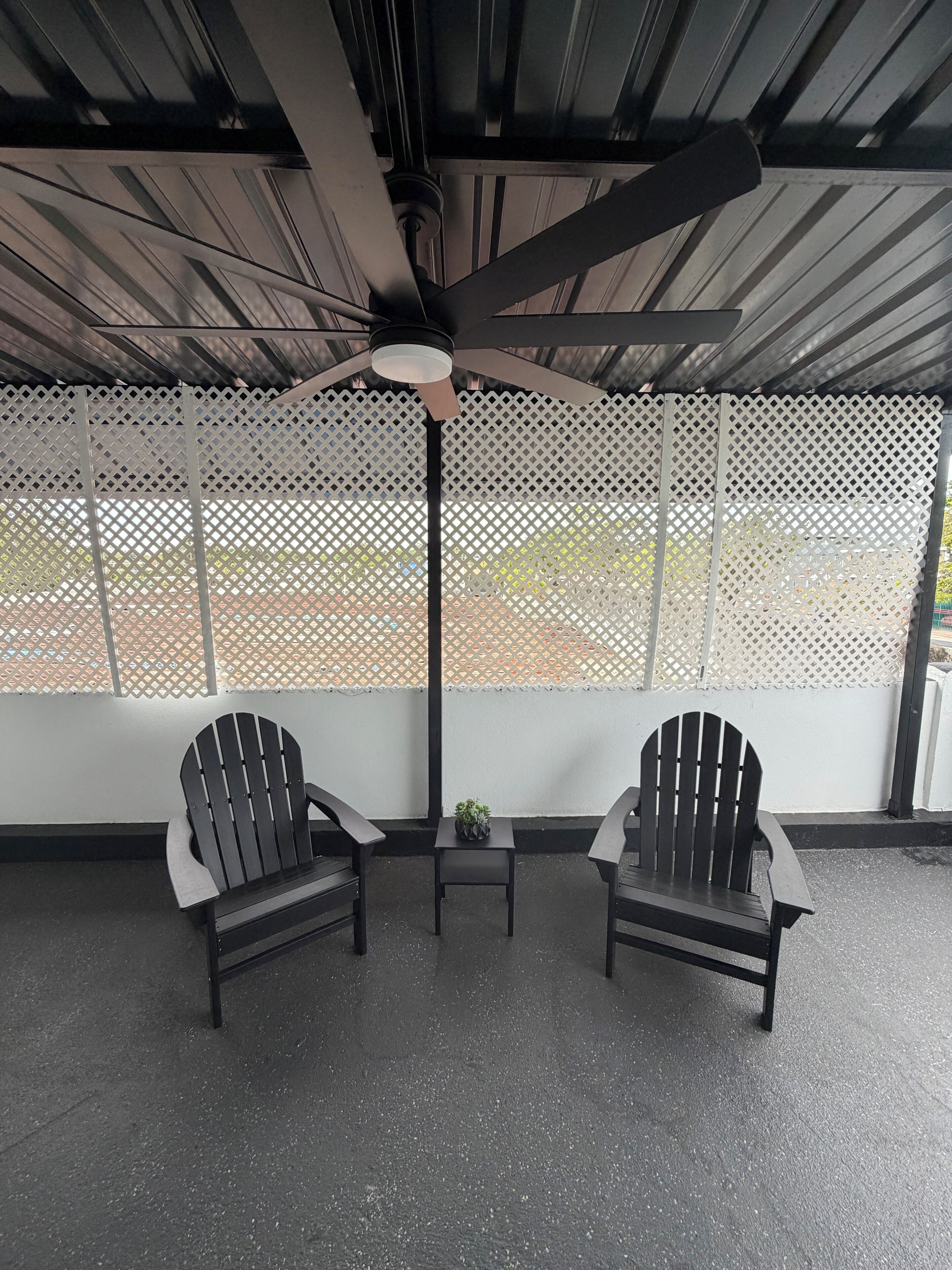 A covered outdoor seating area with two Adirondack chairs, a small table with a plant, and a ceiling fan.