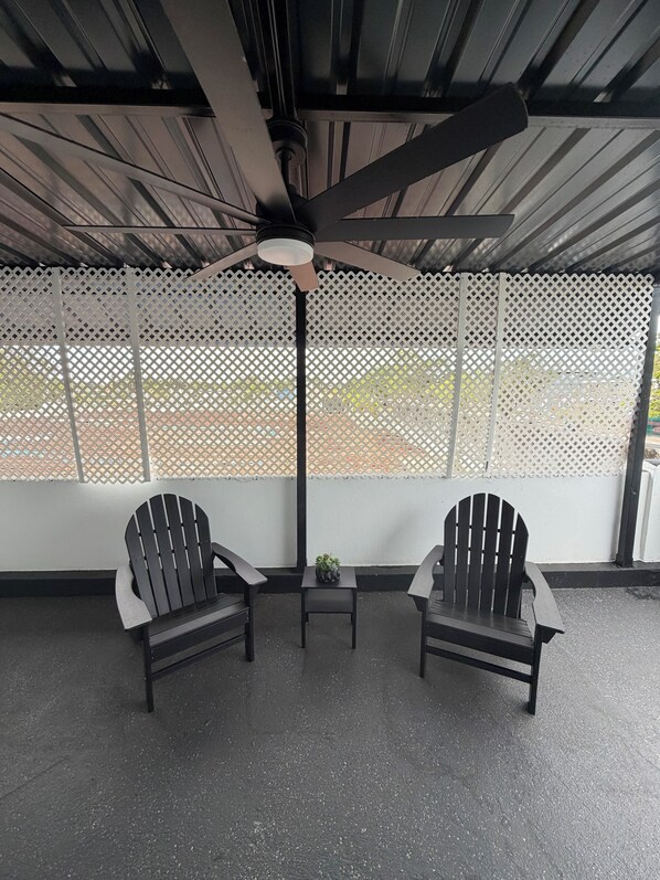 A covered outdoor seating area with two Adirondack chairs, a small table with a plant, and a ceiling fan.