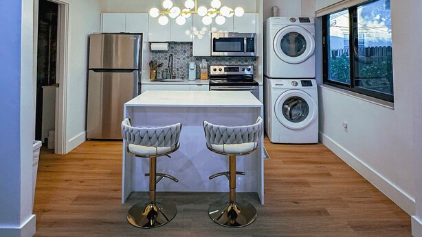 A modern kitchen with a central island, stainless steel appliances, a built-in washing machine, and a large window. - Casa Kiwi in Miami - Sleeps 6 (Miami)