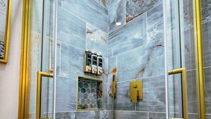 A bathroom with marble tiles, a shower with a gold faucet, and a hexagonal window. - Casa Kiwi in Miami - Sleeps 6 (Miami)