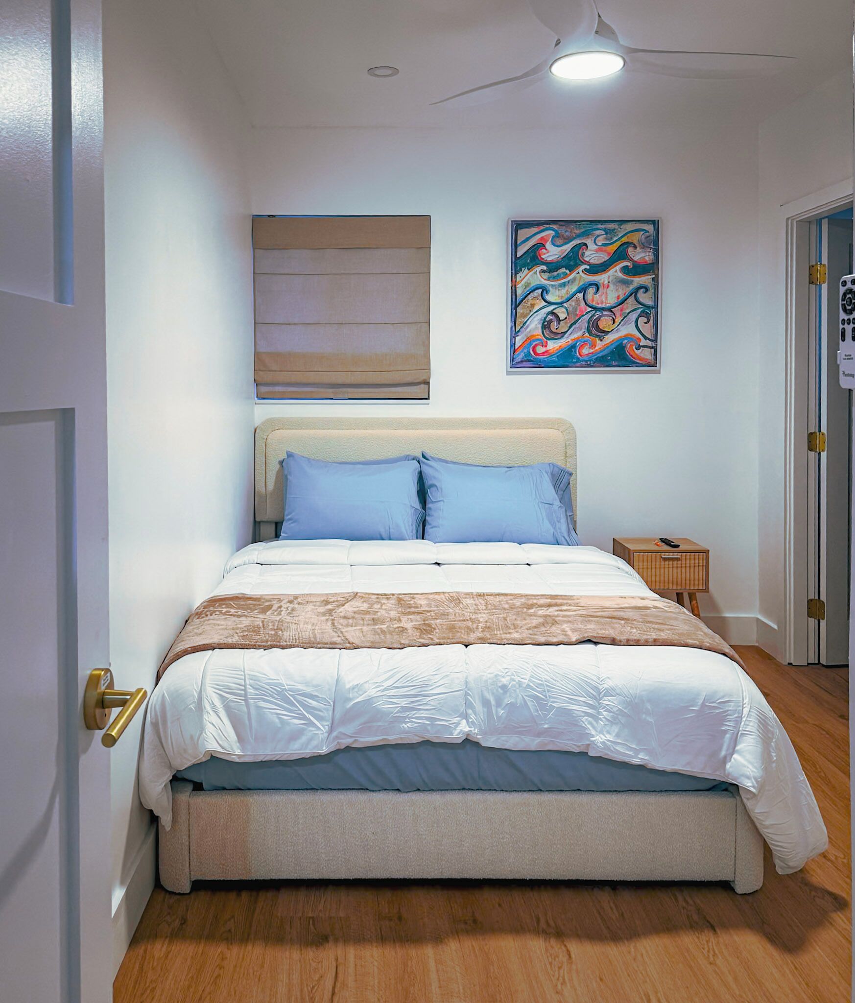 Une chambre à coucher avec un lit, une table de chevet, un tableau et un ventilateur de plafond.