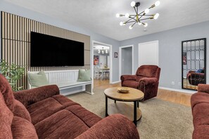 Ein modernes Wohnzimmer mit großem Flachbildfernseher, roten Sofas, einem Holztisch und einer außergewöhnlichen Deckenleuchte.