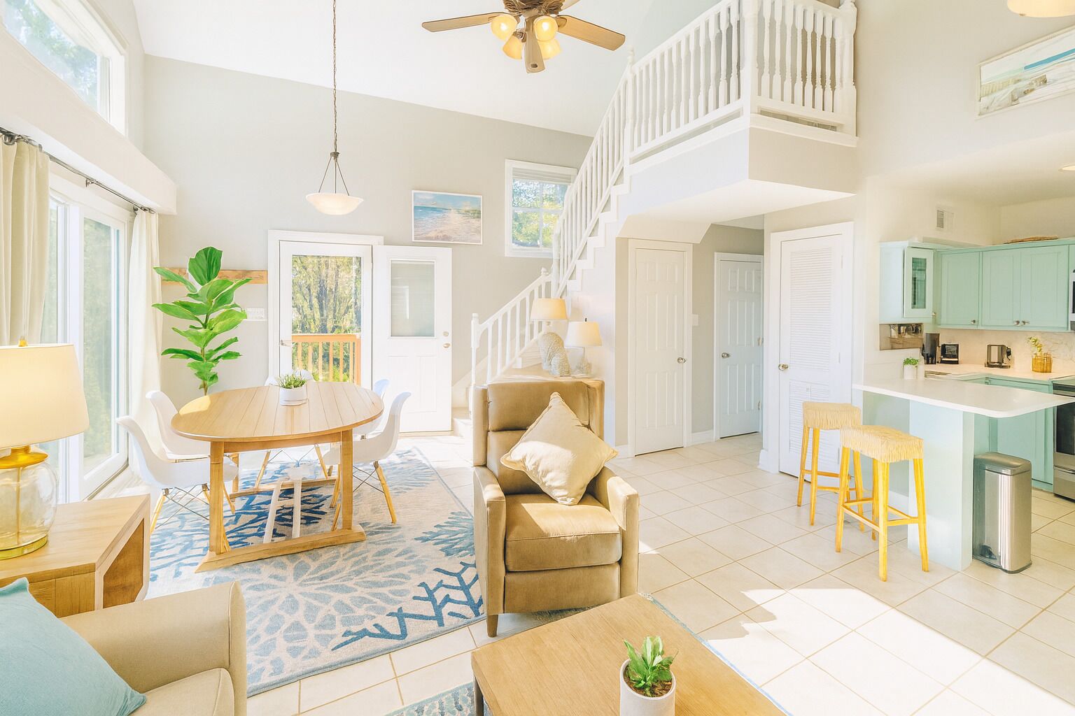 A spacious living room with a high ceiling, a dining area, a kitchen, and a staircase leading to an upper level.