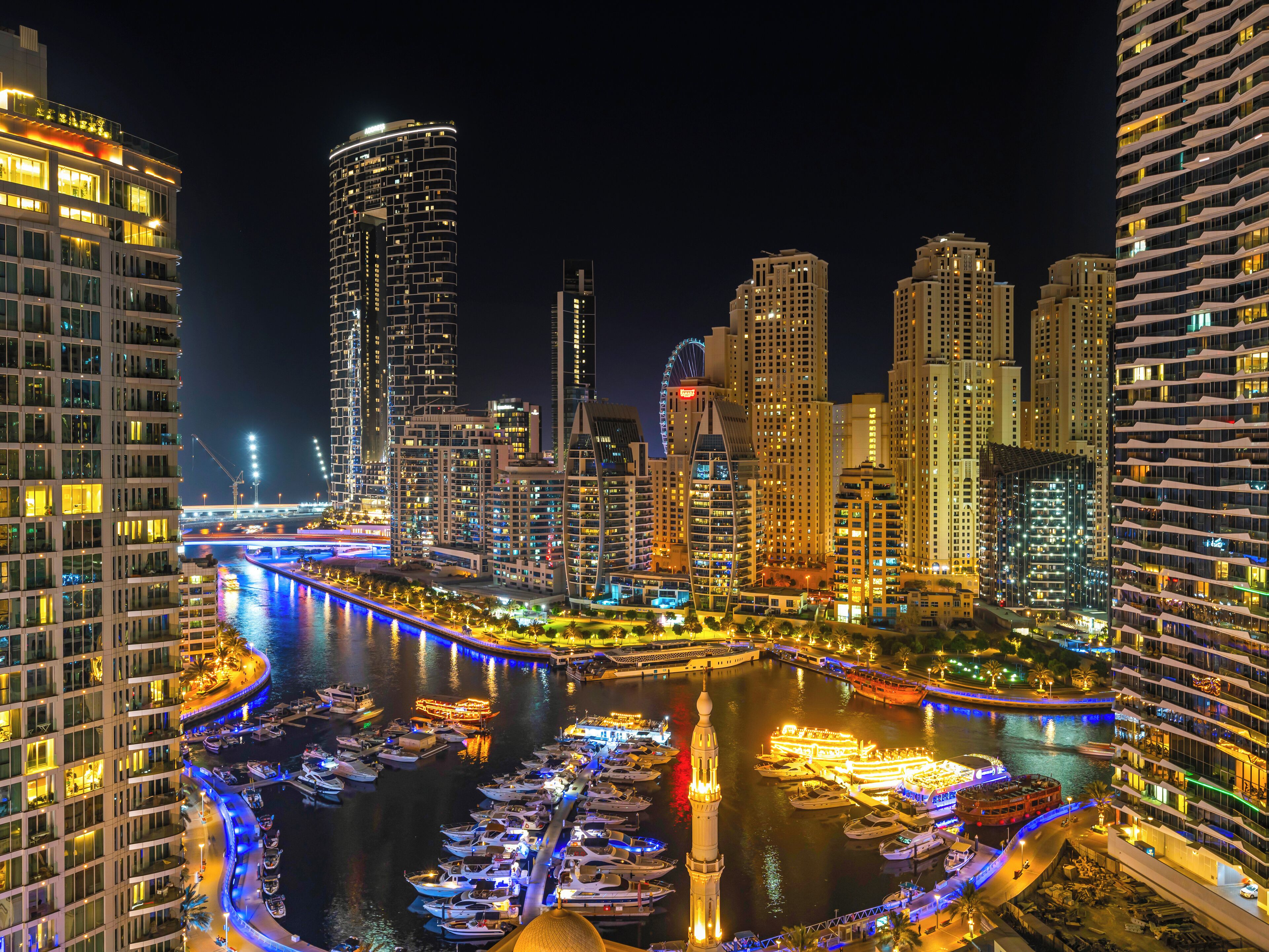 A nighttime cityscape with high-rise buildings, a river, and a marina with boats. - Centric Flat with Marina View (Dubai)