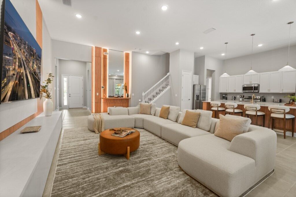 A modern living room with a sectional sofa, a coffee table, and a kitchen area with white cabinets and a bar.