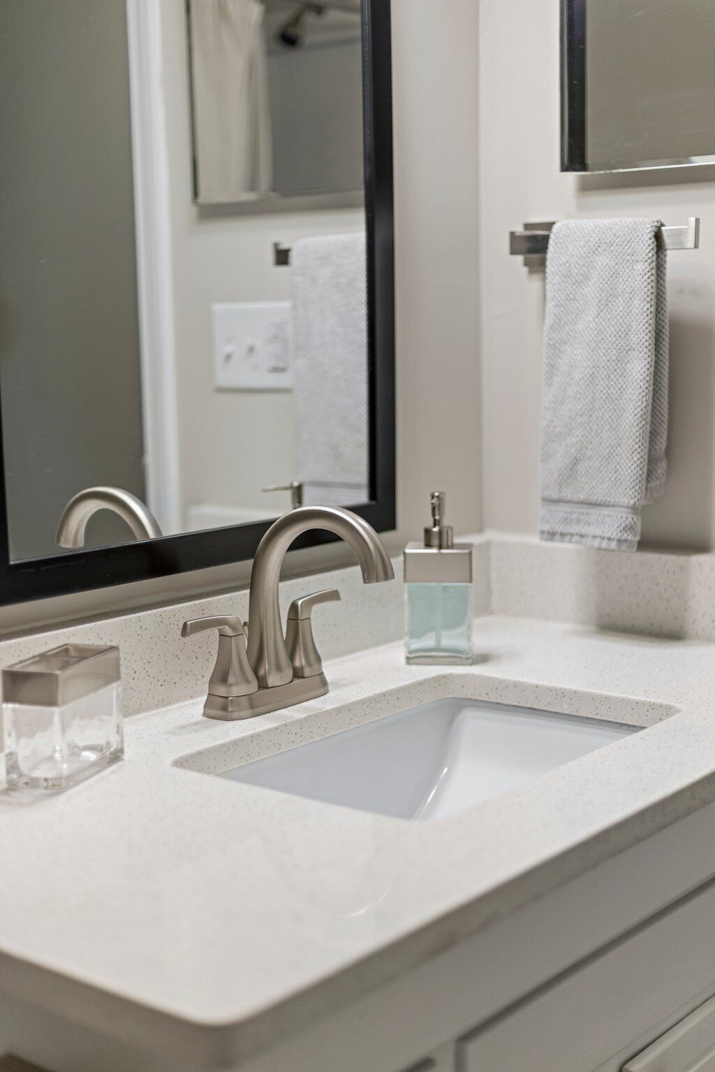Une salle de bain avec un lavabo blanc, un robinet moderne, un distributeur de savon en verre et une serviette suspendue à un porte-serviettes.