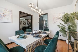 Ein Essbereich mit einem Marmortisch, Smaragdgrün-Stühlen und einem modernen Kronleuchter.