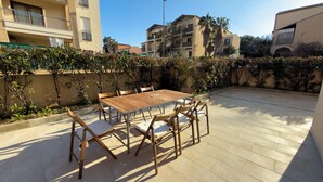 Patio esterno con tavolo e sedie in legno, circondato da un muretto con piante rampicanti.