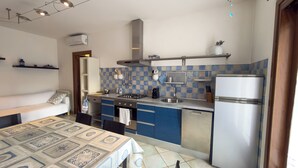 Cucina compatta con piano cottura a gas, lavello e frigorifero. Un tavolo da pranzo con tovaglia fantasia.