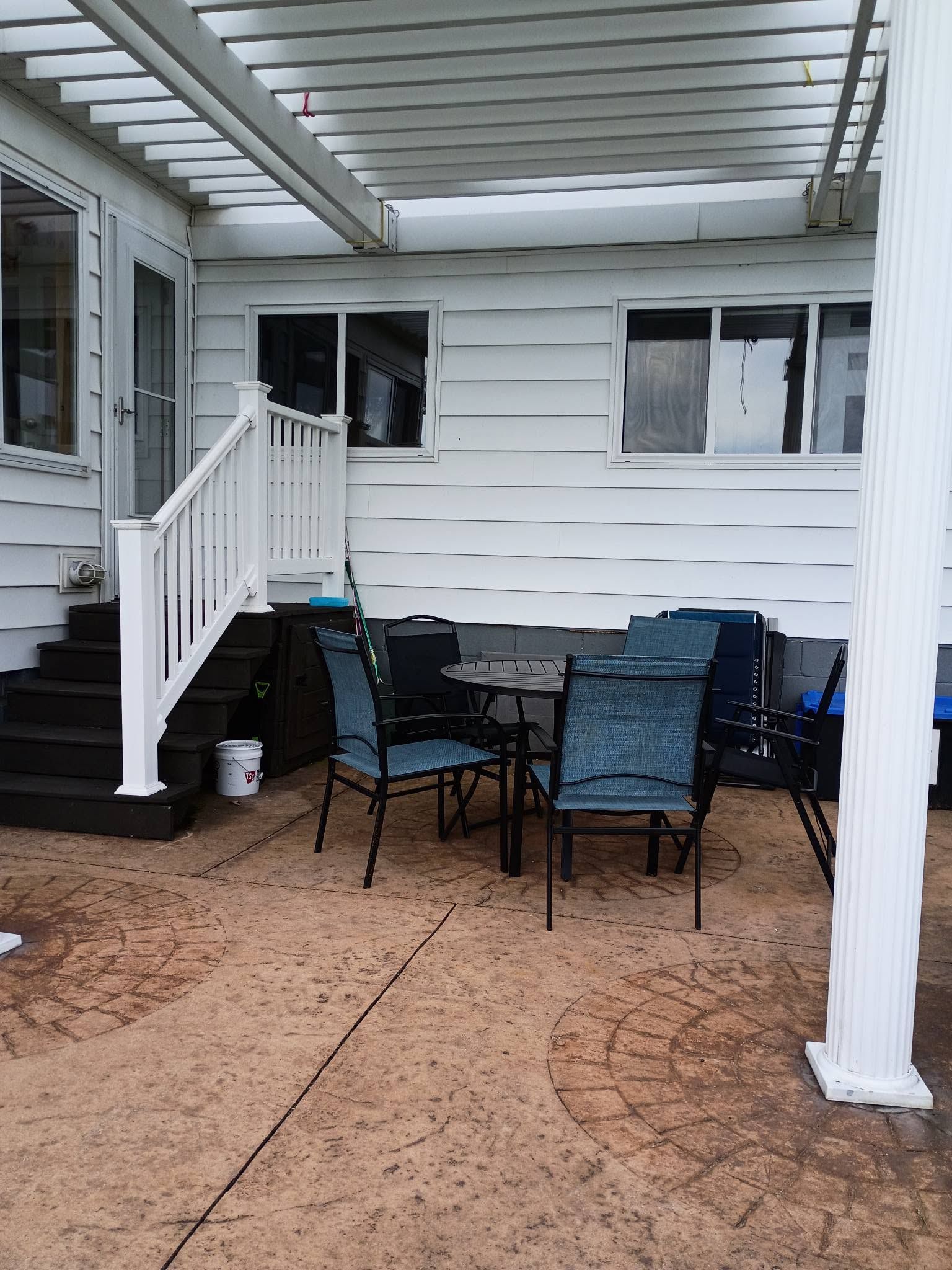 A covered patio area with a dining table and chairs, a staircase leading to the house, and a white railing.