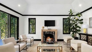 A modern living room with a fireplace, comfortable seating, and large windows offering a view of the outdoors.