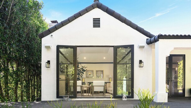 A modern house with a large glass door leading to a dining area with a table and chairs.