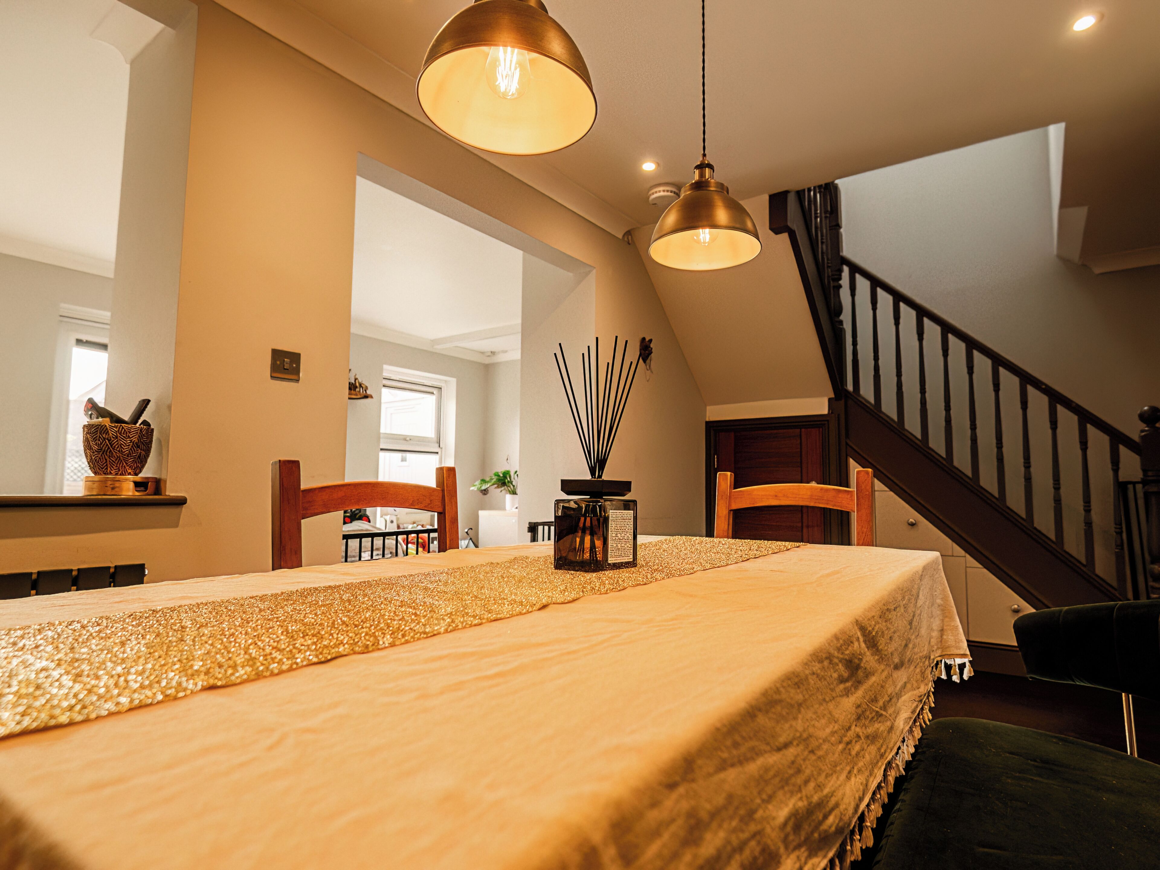 A dining area with a table set for two, a chandelier, and a staircase leading to an upper level.