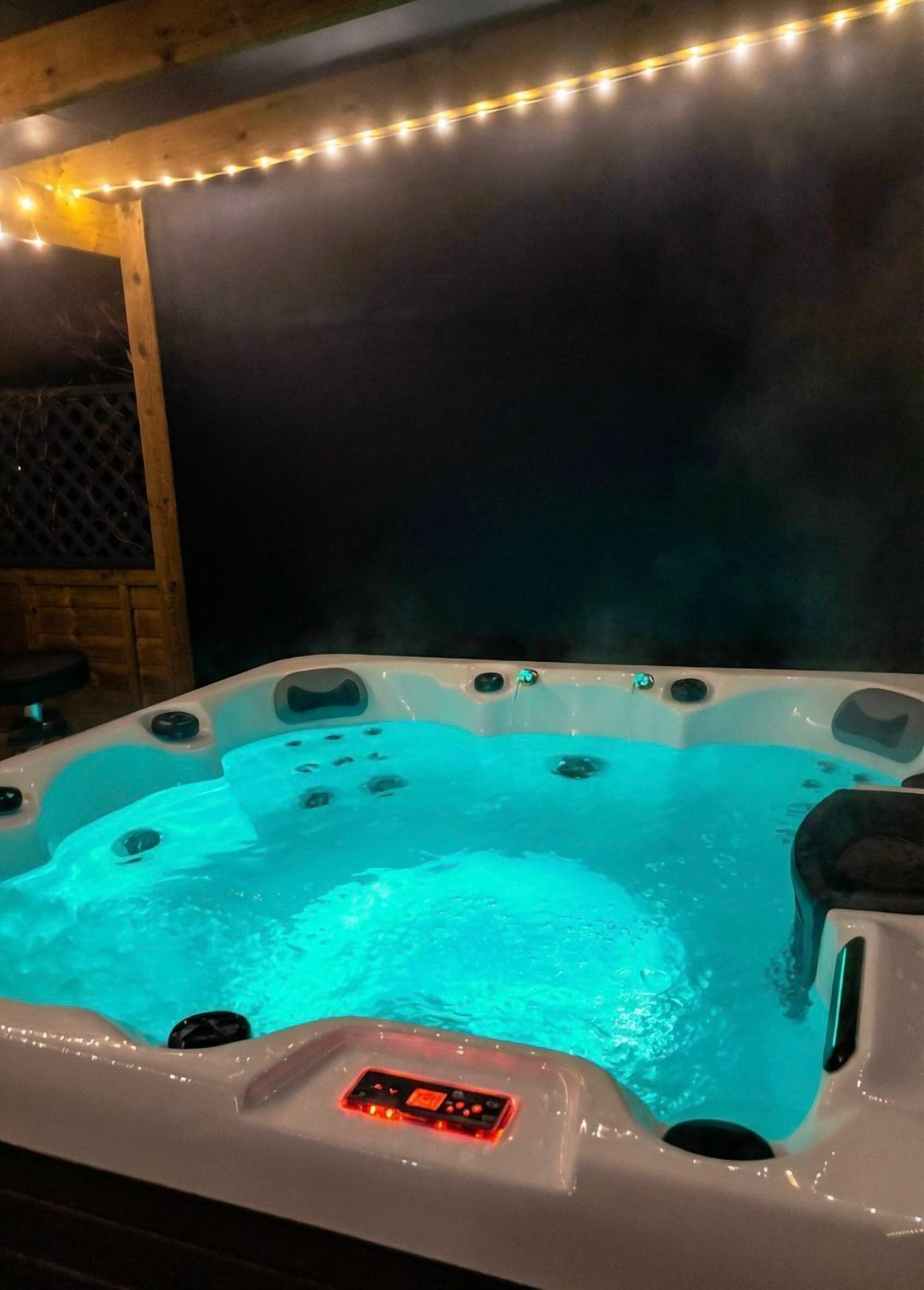 A hot tub with a control panel, surrounded by a wooden deck and string lights.