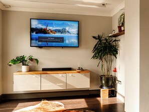 A flat-screen TV mounted on a wall, a wooden console table with a potted plant, and a large potted plant beside the console. - Sun Set House with Hot Tub (Witchford)