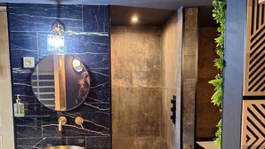 A modern bathroom with a marble sink, a round mirror, a gold-colored vessel, a shower, and a black furry rug on the floor.