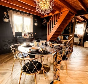 Un coin repas avec une table ronde dressée pour six personnes, entourée de six chaises au design original. On aperçoit un escalier au fond, qui mène à un niveau supérieur.
