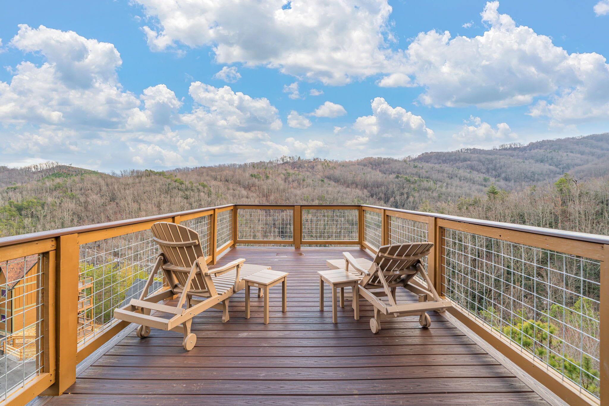 Eine Holzterrasse mit zwei Liegestühlen und einem Tisch, mit Blick auf eine bewaldete Landschaft.