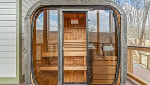 Een sauna met houten banken en een glazen deur, gelegen op een houten terras met uitzicht op bomen.