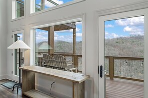 A spacious room with a large wooden table, a chair, and a view of a forested landscape through large windows. - New & Lux Hottub, Sauna with Mt Views - Otter Run #4 (Gatlinburg)