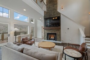A spacious living room with a fireplace, large windows, and a high ceiling. - New & Lux Hottub, Sauna with Mt Views - Otter Run #4 (Gatlinburg)
