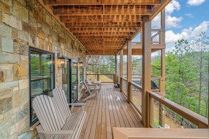 A wooden deck with Adirondack chairs and a table, overlooking a forested area. - Luxury Home w Hot Tub & Mt Views - Otter Run #2 (Gatlinburg)