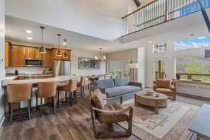 A spacious living area with a kitchen, bar seating, and a balcony with a view. - Luxury Home w Hot Tub & Mt Views - Otter Run #2 (Gatlinburg)