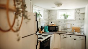 A kitchen with white brick walls, a stove, a microwave, a sink, and potted plants.
