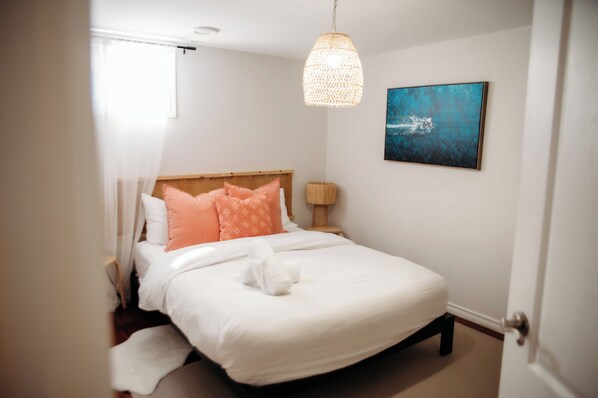 A neatly made bed with white and peach pillows, a white towel, and a hanging light fixture.