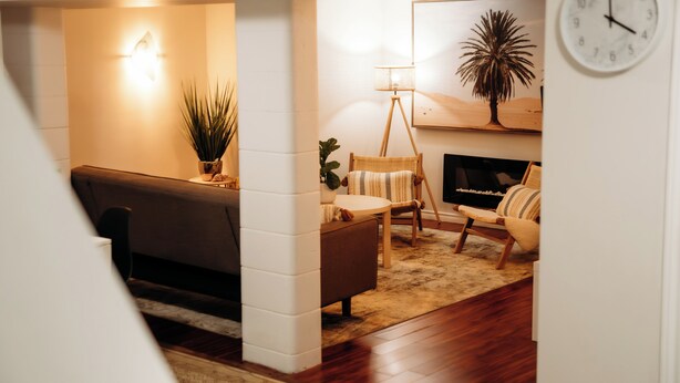 A cozy living room with a sofa, a chair, a small table, and a floor lamp. There is a wall clock and a framed picture on the wall.