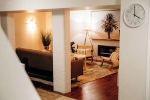 A cozy living room with a sofa, a chair, a small table, and a floor lamp. There is a wall clock and a framed picture on the wall. - Cozy Fall Getaway | 2 Queens | Long Stay Ready (Belleville)