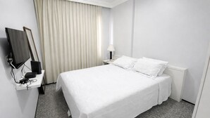 Ein Hotelzimmer mit einem Bett, einem Fernseher, einem Schreibtisch mit Lampe und einem fenster mit Vorhängen.