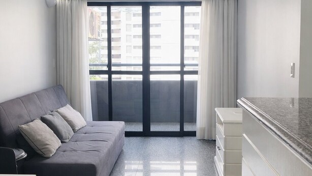 Ein modernes Wohnzimmer mit grauem Sofa, einem kleinen Tisch und einer Küchenzeile mit weißem Schrank.