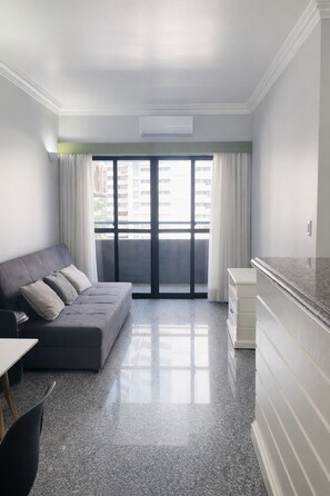 A modern living room with a grey sofa, a small table, and a kitchen area with a white cabinet. - Beachfront Apartment in Fortaleza / Prime Location Near the Beach (Fortaleza)