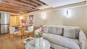 A modern living room with a sofa, dining table, chairs, a refrigerator, and a decorative vase. - Amazing Apartment in Center of Paris (Paris)
