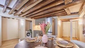 A dining area with a wooden table set for four, surrounded by chairs. A pink vase with flowers is on the table. - Amazing Apartment in Center of Paris (Paris)