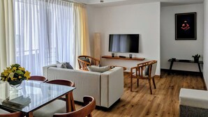 A modern living room with a sofa, chairs, a TV, and a dining table with a vase of flowers. - 3-bedroom apartment in peaceful Colombo with AC, gym and pool access (Colombo)