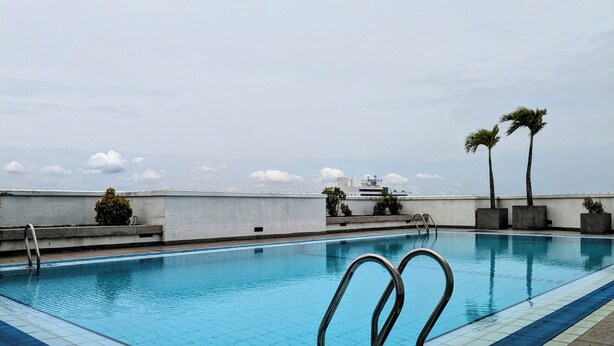 A rooftop swimming pool with clear blue water, a lifeguard chair, and two palm trees. - 3-bedroom apartment in peaceful Colombo with AC, gym and pool access (Colombo)