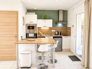 A modern kitchen with a wooden table, white chairs, a stainless steel oven, and a green accent wall.