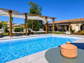 A swimming pool with lounge chairs, a pergola, and a house in the background.