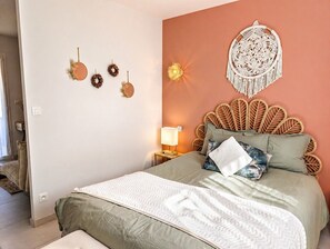 A bedroom with a bed, a wall-mounted macrame wall hanging, and a nightstand with a lamp.