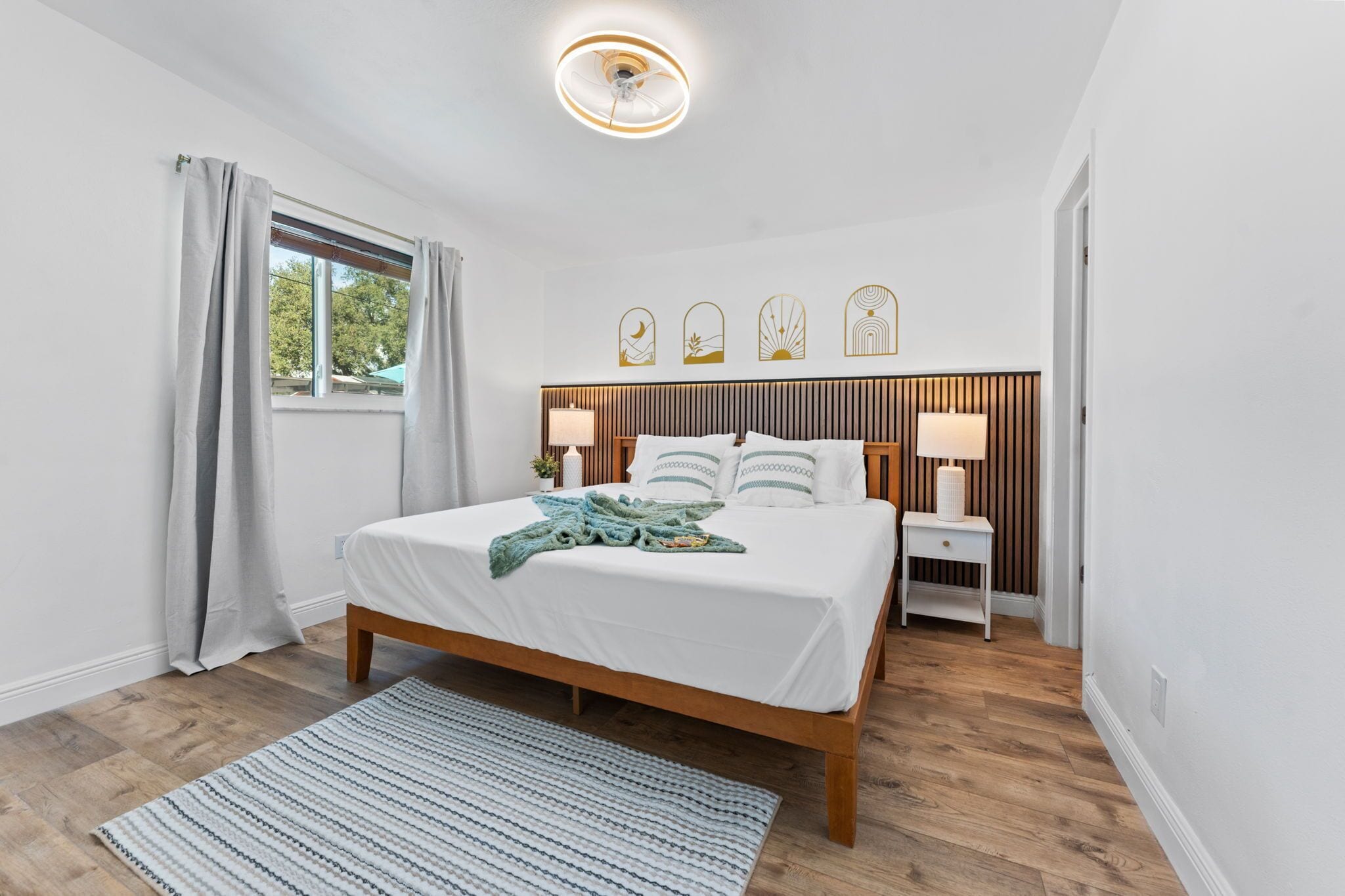 Un dormitorio moderno con una cama de madera, una mesita de noche con lámpara y una ventana con cortinas.