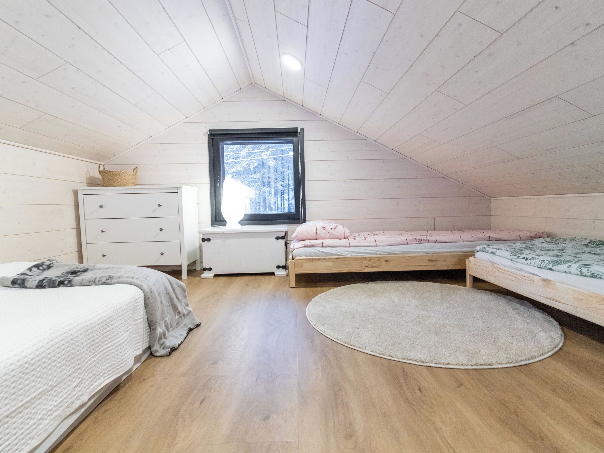 Un dormitorio ático acogedor con dos camas de madera, un aparador blanco y una ventana con vistas a árboles.